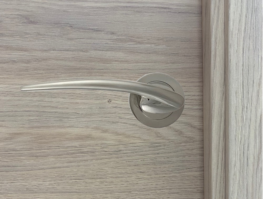 Manilla de zamak con roseta redonda en acabado níquel satinado para puertas de madera clara